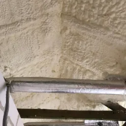 Poddasze ocieplone pianką, widoczne rury wentylacyjne owinięte folią aluminiową i fragment konstrukcji drewnianej