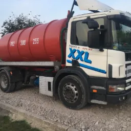 Ciężarówka asenizacyjna Scania 94D z pomarańczową cysterną na gruzowym podłożu, z widocznymi numerami 782, 300, 255 na cysternie i logo firmy logistik in BIPO-BUD S.C. XXL lasttrans gmbh.