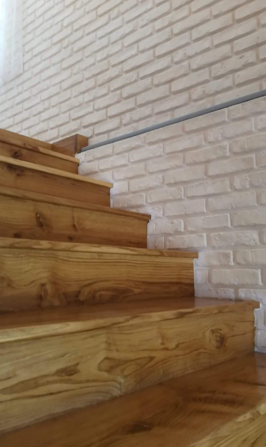 Drewniane schody z widocznym usłojeniem na tle ściany z cegły w Warszawie.