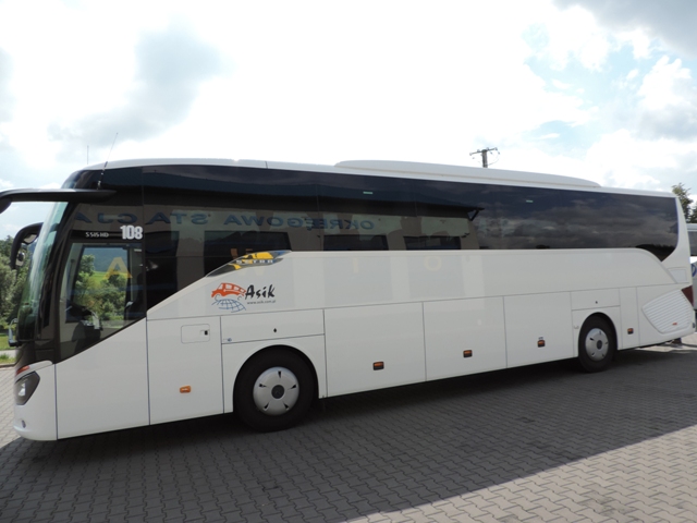 Biały autokar turystyczny z logo firmy 'Asik' na boku, zaparkowany na kostce brukowej w słoneczny dzień.