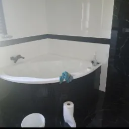 Narożna wanna z czarną mozaiką w łazience w Pszczynie, widoczne akcesoria i niebieska szmatka, przygotowana do dalszych prac wykończeniowych.