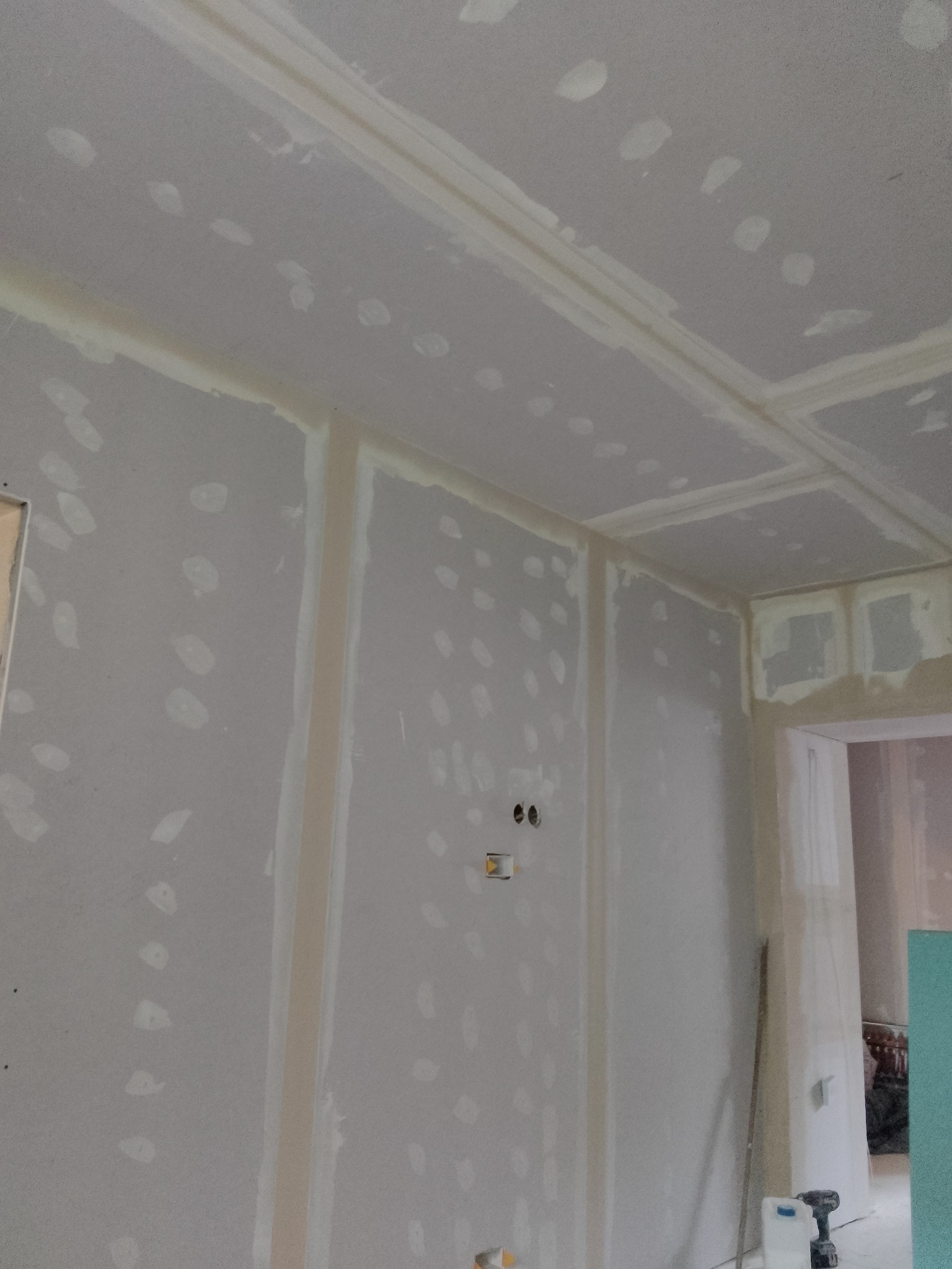 Wnętrze w trakcie prac wykończeniowych: ściany i sufit pokryte płytami kartonowo-gipsowymi, z widocznymi miejscami łączeń i szpachlowania, przygotowane do dalszych etapów prac malarskich.