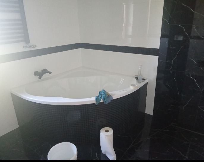 Narożna wanna z czarną mozaiką w łazience w Pszczynie, widoczne akcesoria i niebieska szmatka, przygotowana do dalszych prac wykończeniowych.