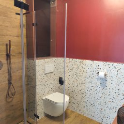 Lubarski Krzysztof - Nowoczesna łazienka z kabiną prysznicową typu walk-in, toaletą podwieszaną i płytkami lastryko na ścianie. Drewnopodobne płytki na podłodze i czerwona ściana.