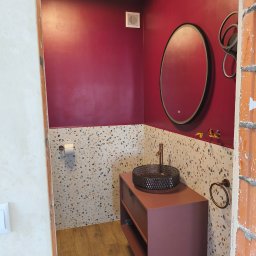 Lubarski Krzysztof - Nowoczesna łazienka w trakcie wykańczania: bordowe ściany, mozaika na ścianie, umywalka na szafce w kolorze bordo, okrągłe lustro z podświetleniem.