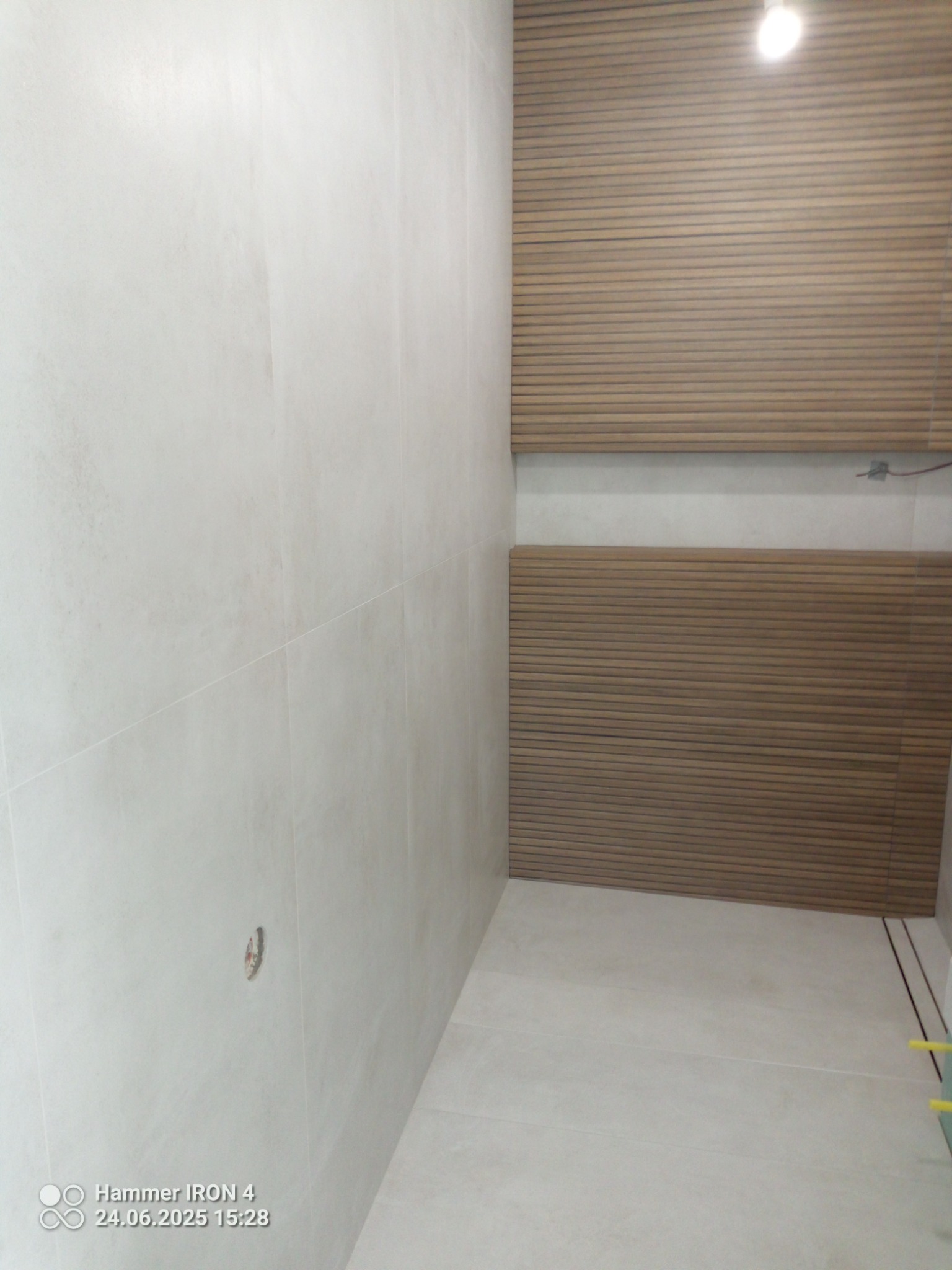 Wykończona łazienka: jasne płytki na ścianach, drewnopodobne lamele na części ściany, minimalistyczny design, widoczny odpływ liniowy.