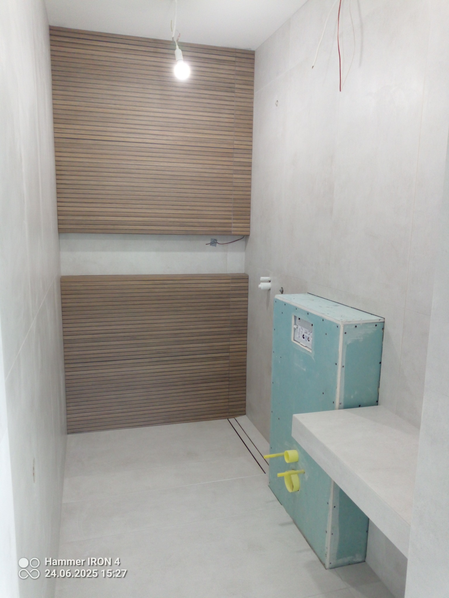 Wnętrze łazienki w trakcie prac: ułożone płytki imitujące drewno na ścianie, zabudowa stelaża WC z płyt GK, jasne płytki podłogowe i ścienne. Widoczne elementy instalacji.