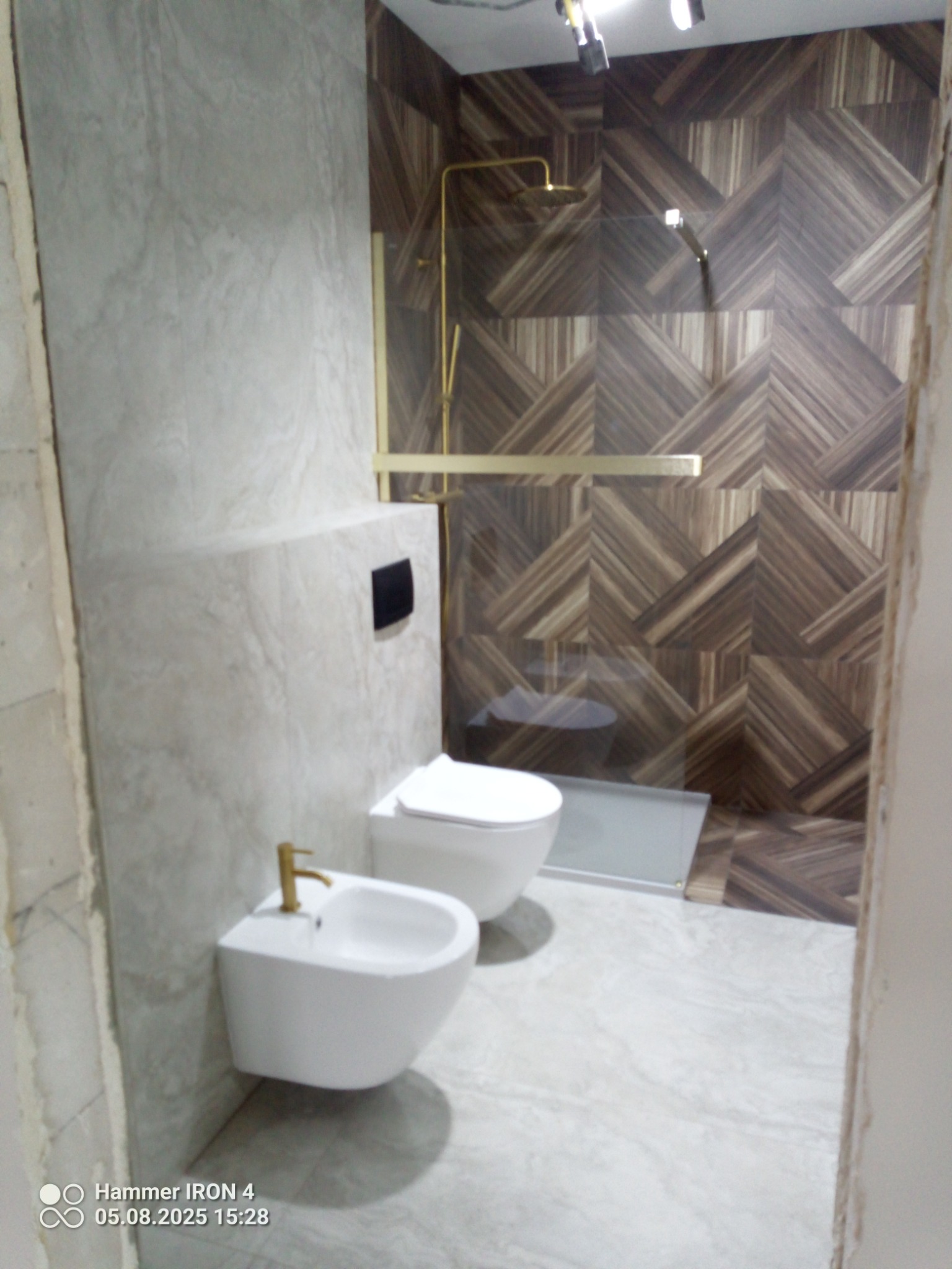 Nowoczesna łazienka po remoncie: biała ceramika, złota armatura i geometryczne płytki w odcieniach brązu. Minimalistyczny design z akcentem luksusu.