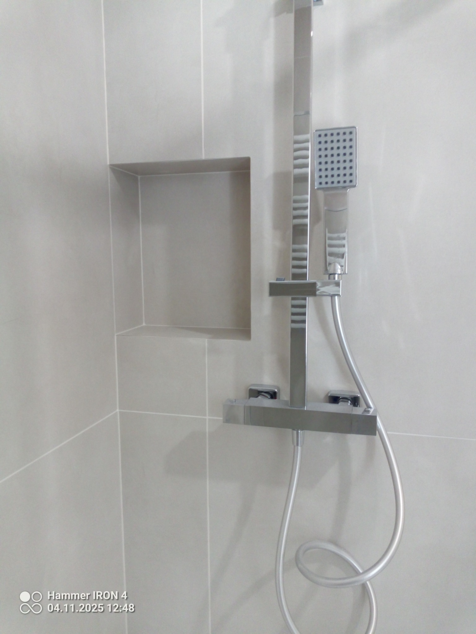 Minimalistyczna łazienka z szarymi płytkami i nowoczesną, chromowaną armaturą prysznicową z deszczownicą oraz wnęką w ścianie wyłożoną płytkami.