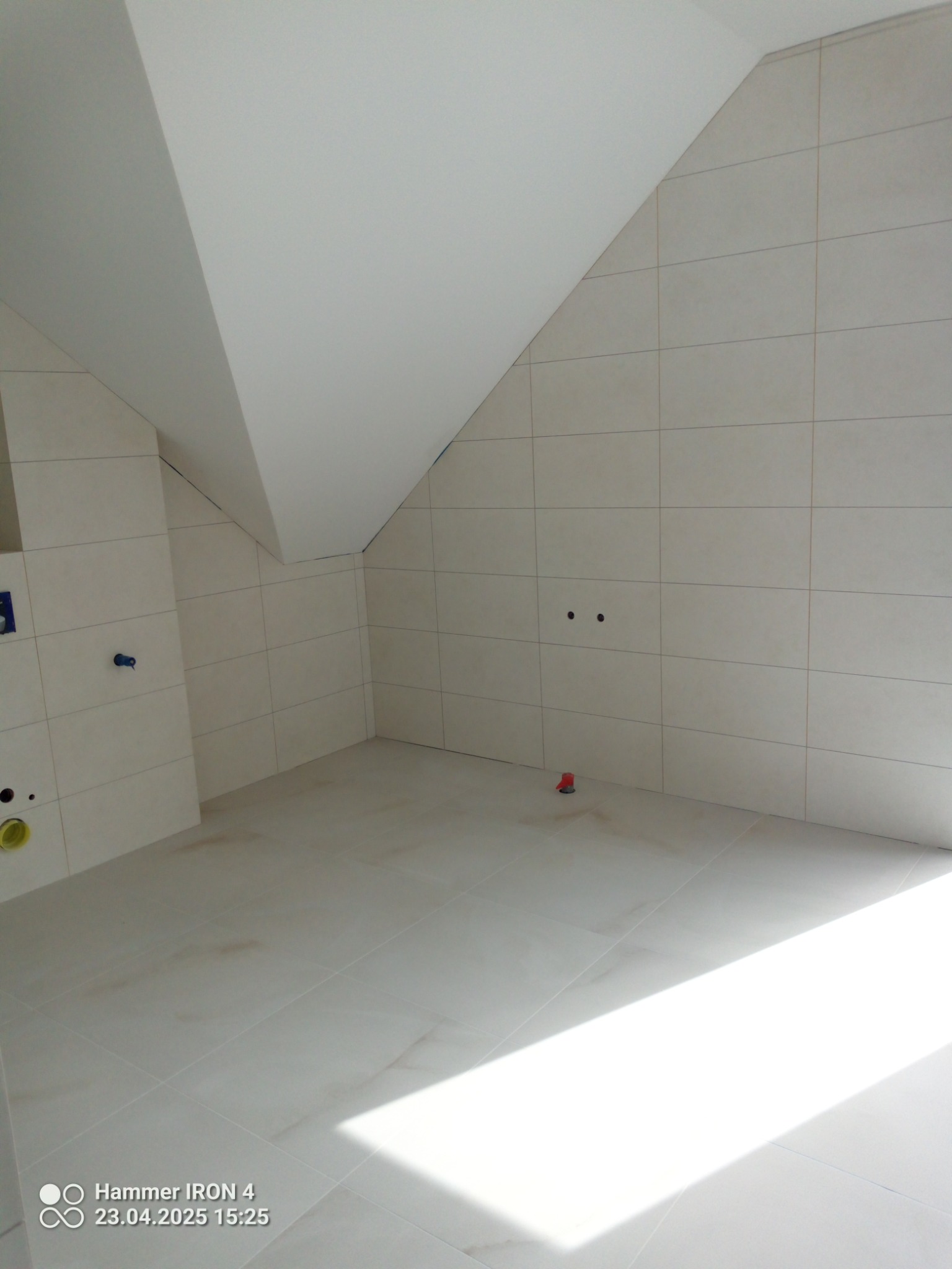 Jasna łazienka na poddaszu po remoncie. Ułożone płytki na podłodze i ścianach, widoczne punkty instalacji. Minimalistyczny styl, świeżo po wykończeniu.