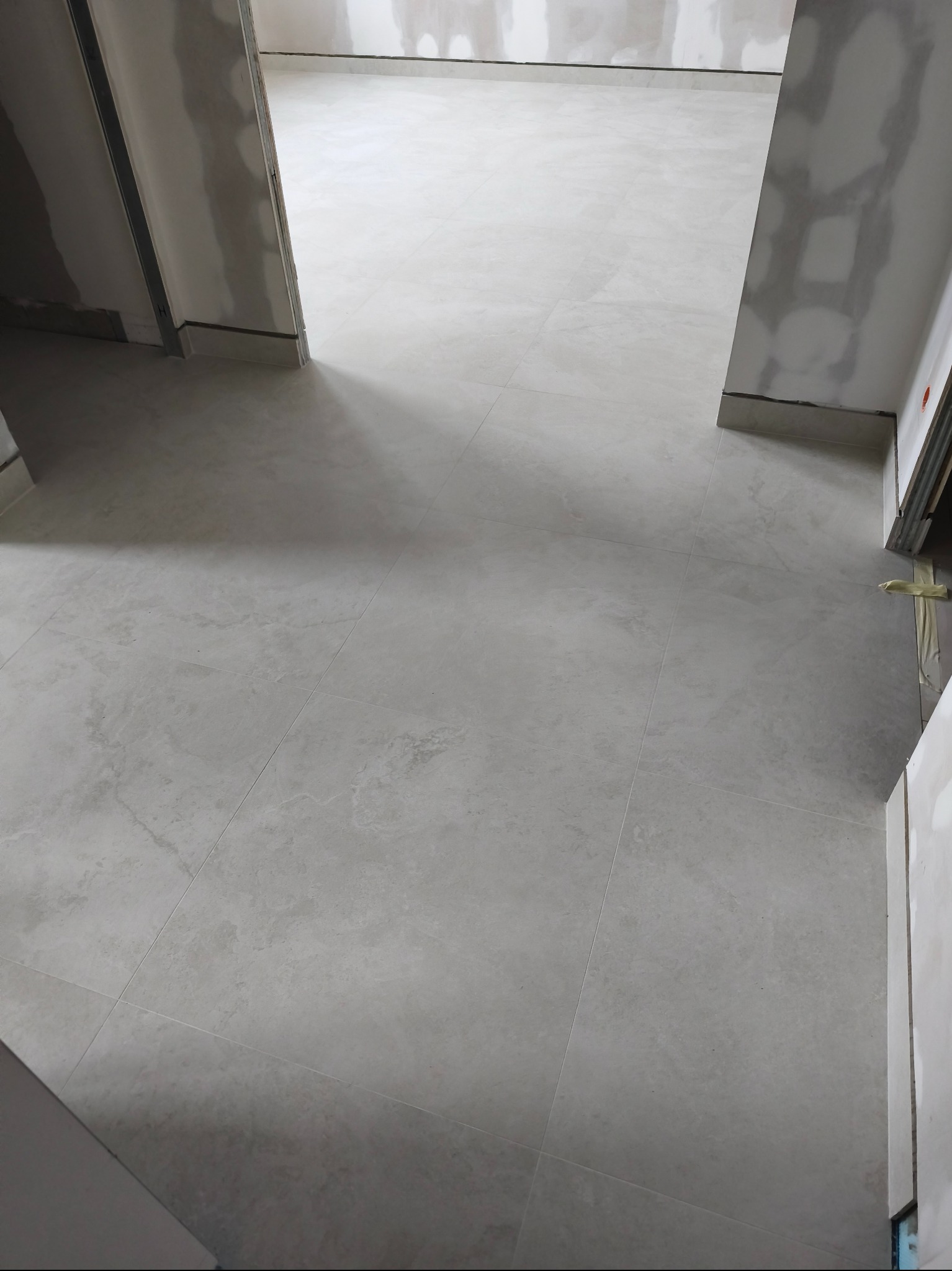 Jasne, matowe płytki podłogowe ułożone w nowym wnętrzu w Warszawie. Widoczne fragmenty ścian przygotowane do malowania. Minimalistyczny design.