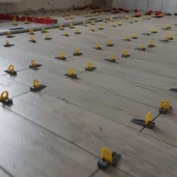 Układanie paneli podłogowych z wykorzystaniem systemu poziomowania płytek w Słupsku, widoczny poziomica i kliny dystansowe.