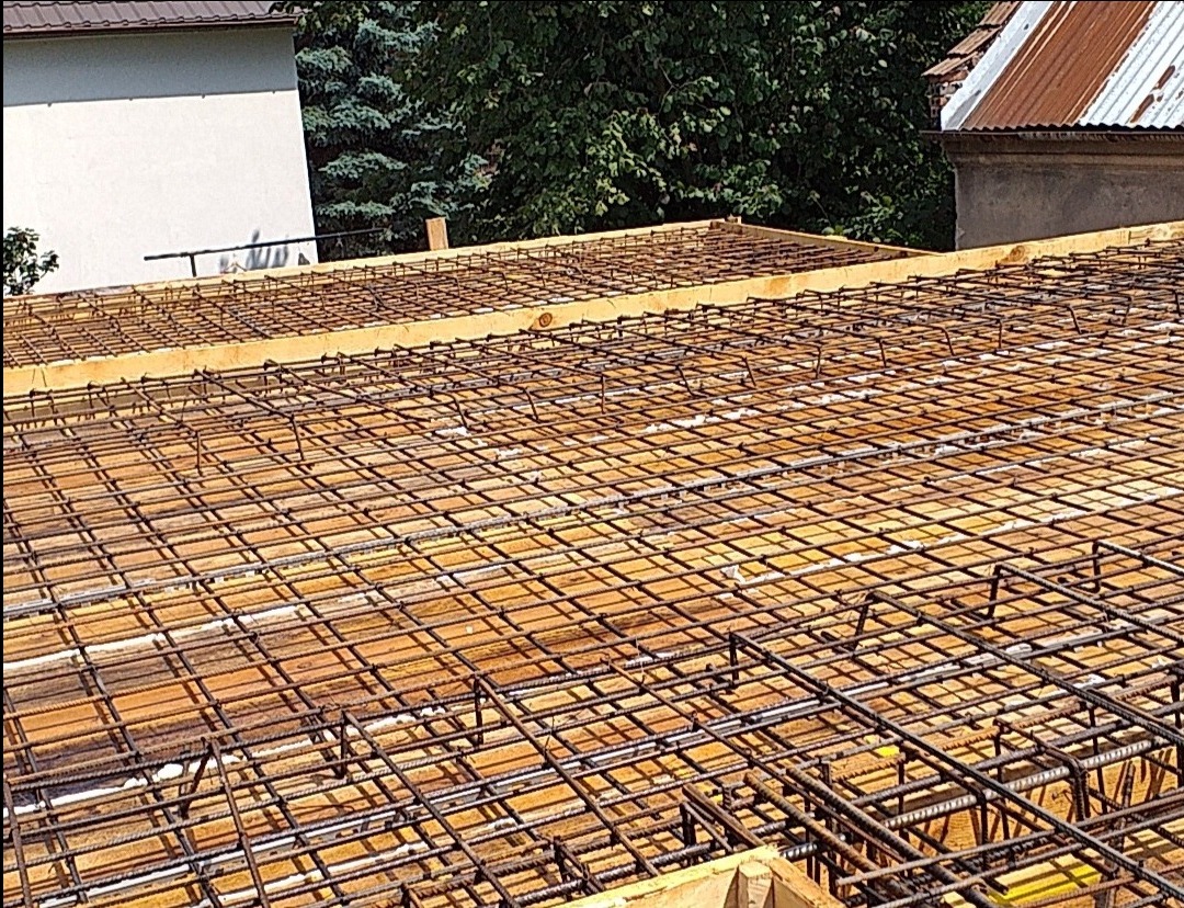 Siatka zbrojeniowa ułożona na drewnianym szalunku, przygotowana do zalania betonem, widok z góry na budowę.