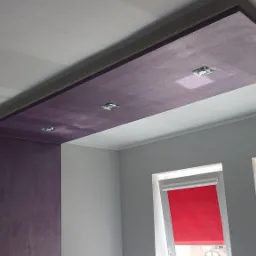 Fioletowy, podwieszany sufit z trzema punktowymi lampami w szarym pokoju z czerwonymi roletami.