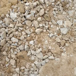 Kruszywo o zróżnicowanej granulacji, od drobnego piasku po większe kamienie o nieregularnych kształtach i szarym zabarwieniu, rozsypane na ziemi.