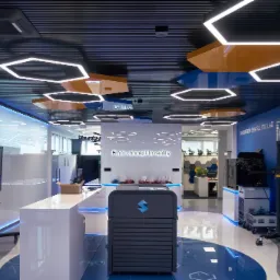 Nowoczesne wnętrze biurowe w Białymstoku z heksagonalnym oświetleniem sufitowym, białymi meblami z podświetleniem LED, niebieskimi akcentami kolorystycznymi i napisem 'From concept to reality'.