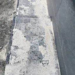 Świeżo ułożona, szara kostka brukowa z pozostałościami piasku kwarcowego do fugowania, przylegająca do ciemnej ściany budynku.