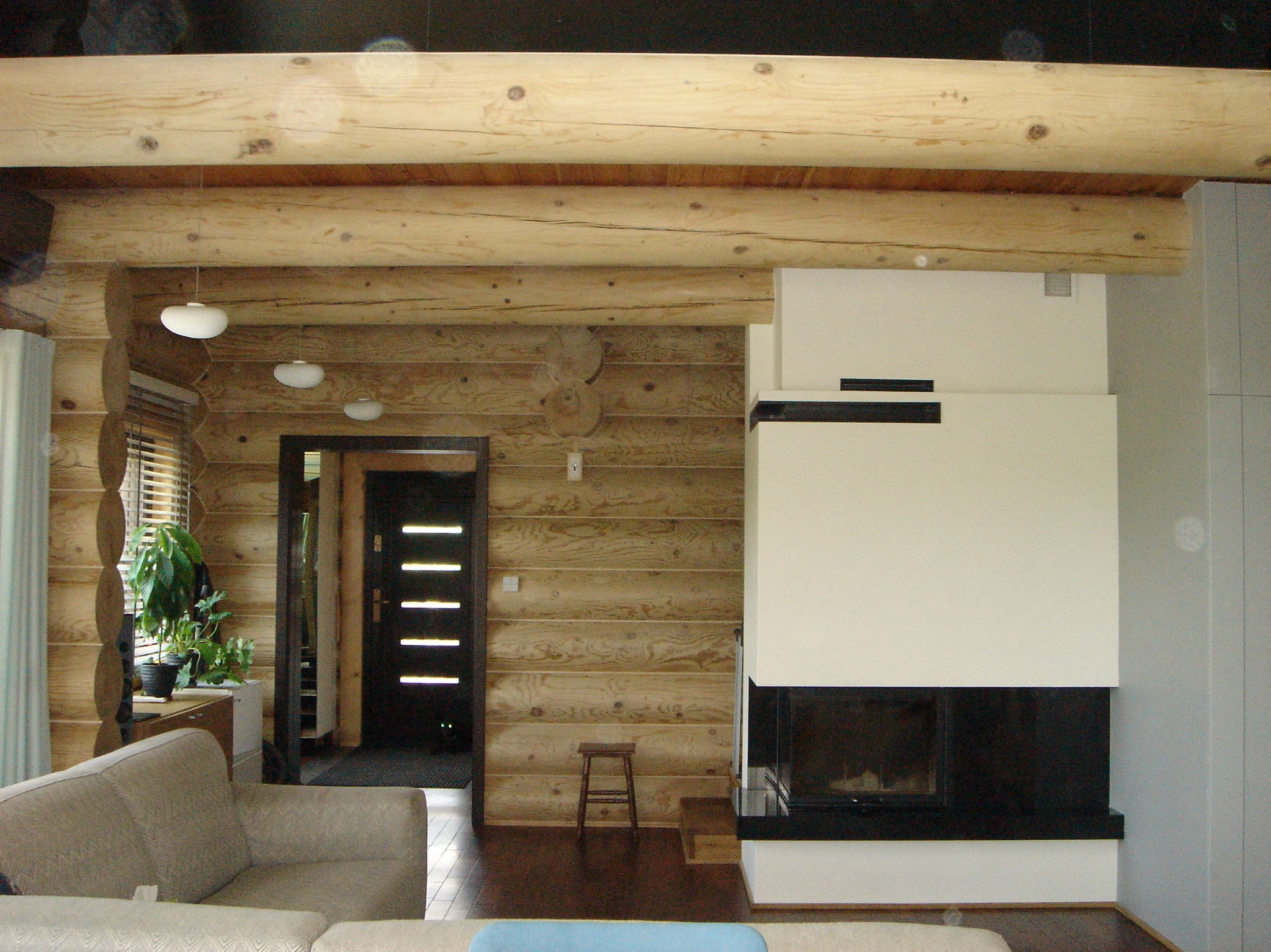 Wnętrze domu z bali z nowoczesnym kominkiem, drewnianą podłogą i widocznym fragmentem sofy.