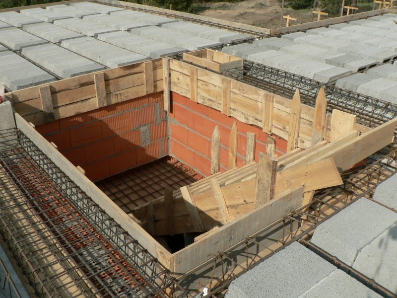 Budowa stropu Teriva: widok z góry na ułożone prefabrykaty betonowe, zbrojenie i drewniane szalunki wokół otworu w stropie wyłożonego cegłą.