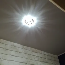 Zamontowana lampa sufitowa z wzorem geometrycznym na tle pomalowanego sufitu i ściany z dekoracyjnej cegły.