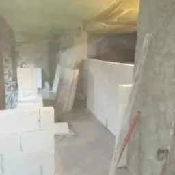 Wnętrze w trakcie budowy z białymi blokami, poziomica oparta o ścianę i folia ochronna na suficie.