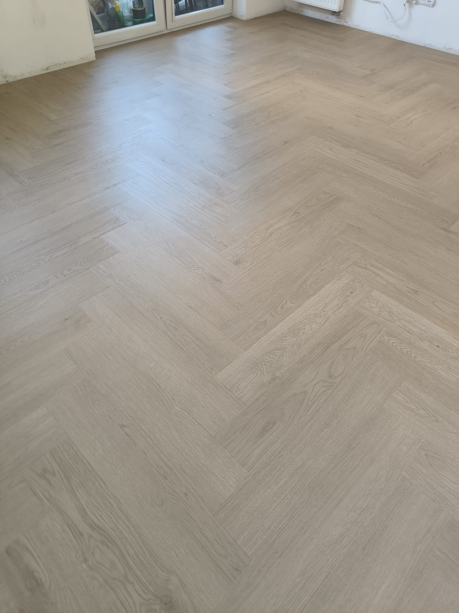 Jasna podłoga ułożona w jodełkę francuską, widok z góry, świeżo po montażu. Naturalny odcień drewna, subtelne słoje. Minimalistyczne wnętrze w tle.