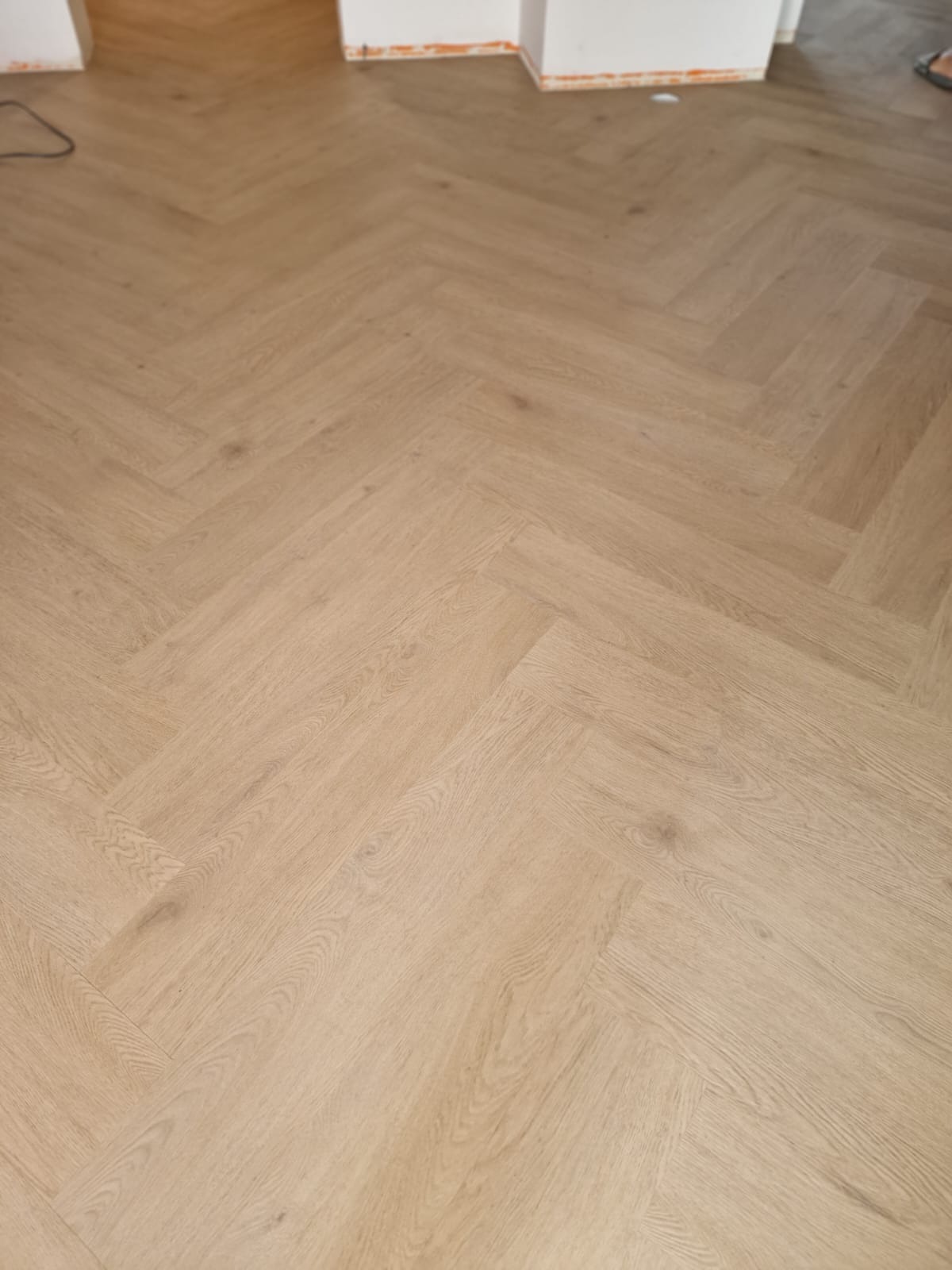 Jasne panele ułożone we wzór jodełki francuskiej, widok z góry. Nowa podłoga w neutralnej kolorystyce, gotowa do użytku.