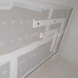 Sufit podwieszany w trakcie montażu, widoczne profile i płyty gipsowo-kartonowe przed szpachlowaniem, zarys konstrukcji w kształcie litery 'Z'.