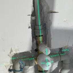 Fragment instalacji wodnej z zaworem w trakcie montażu, wyznaczona pion i poziom zielonym laserem na tle surowej ściany.