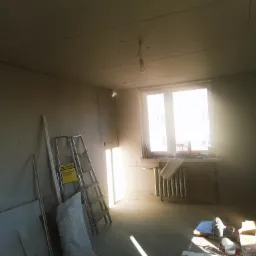 Pokój w trakcie montażu płyt kartonowo-gipsowych, widoczne płyty, drabina aluminiowa, narzędzia i surowe wykończenie ścian z widocznymi łączeniami płyt.