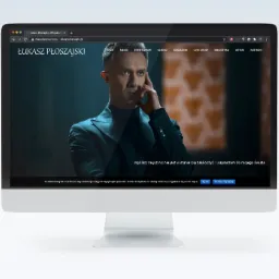 Ekran monitora iMac wyświetlający oficjalną stronę internetową aktora Łukasza Płoszajskiego z jego portretem na tle ciemnej scenografii.