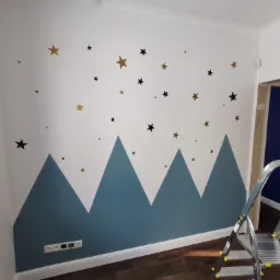 Ściana w pokoju dziecięcym w Nadarzynie z motywem gór i gwiazd, malowana na biało i niebiesko, z widoczną drabiną malarską.