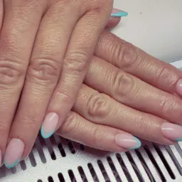 Dłonie z delikatnym manicure hybrydowym: jasnoróżowa baza i turkusowy french na owalnych paznokciach, ułożone na metalowej kratce.