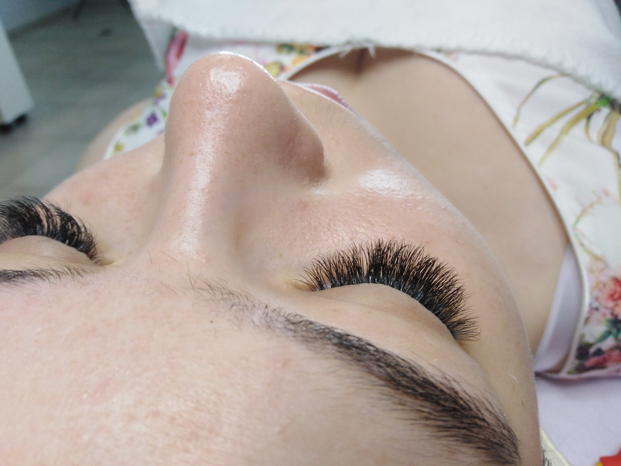 Zbliżenie na twarz kobiety z przedłużonymi rzęsami 2D-3D, widoczne pojedyncze włoski i delikatny makijaż oka, skóra lekko błyszcząca.