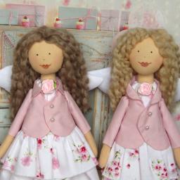 Hobbylandia Sp. z o.o - Dwie ręcznie robione lalki szmaciane anioły w pastelowych różowych marynarkach i kwiecistych sukienkach, stojące na tle dekoracji urodzinowych.