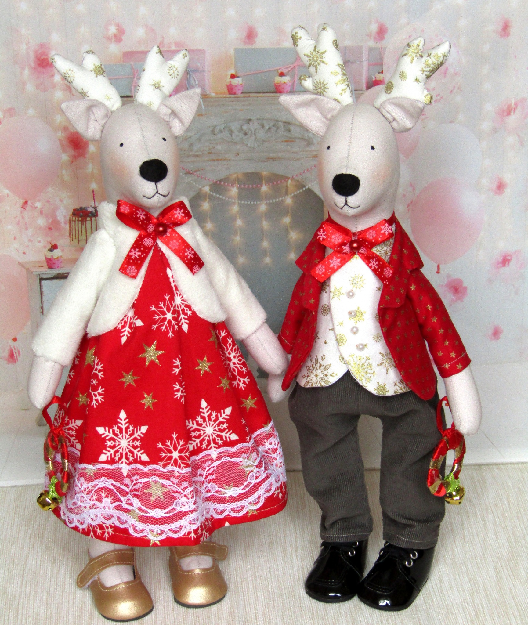 Para ręcznie robionych reniferów w świątecznych strojach: reniferka w czerwonej sukience ze złotymi gwiazdkami i białymi płatkami śniegu oraz renifer w szarych spodniach i czerwonej marynarce ze...