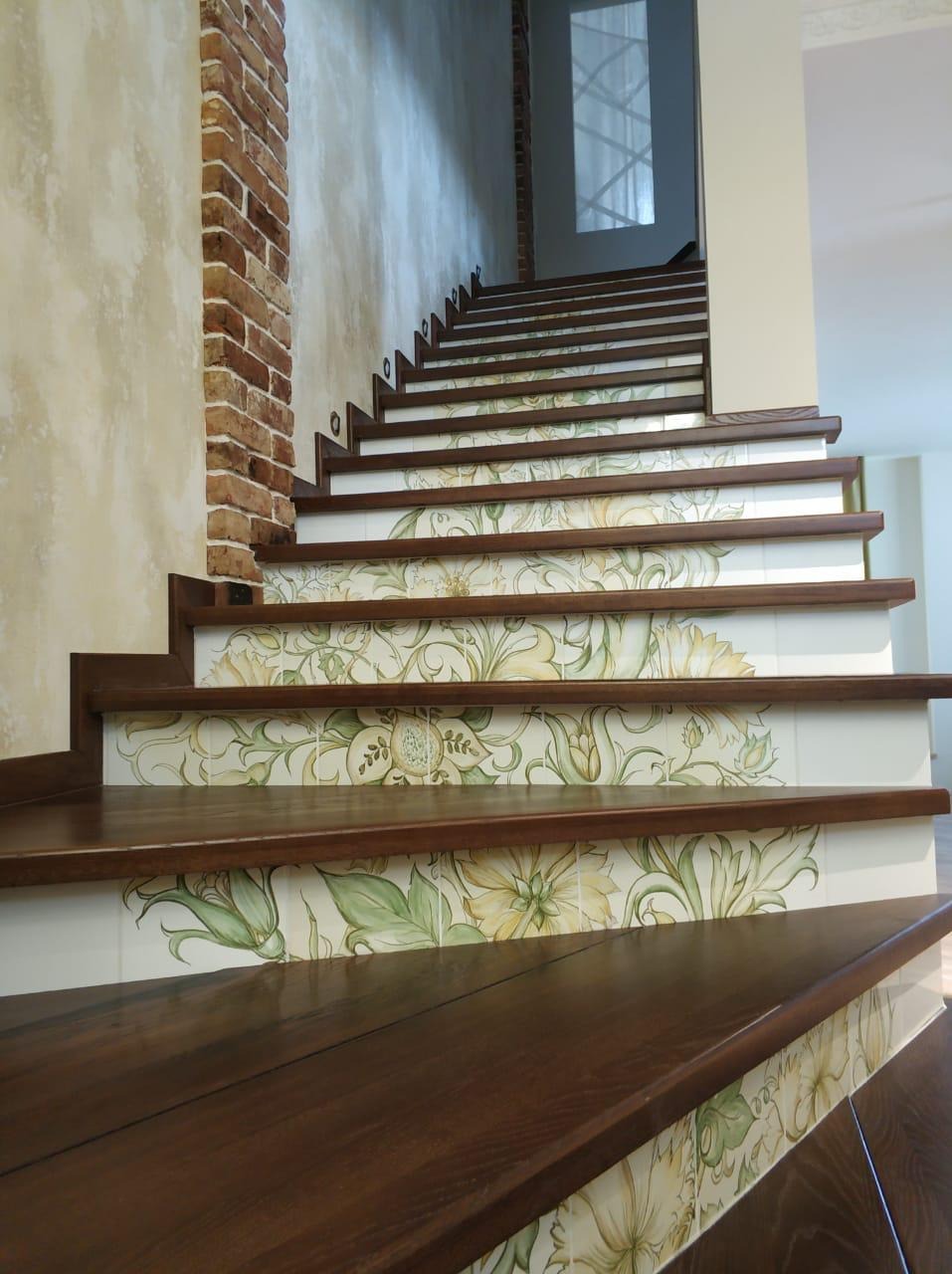 Schody z ciemnego drewna z ceramicznymi płytkami dekoracyjnymi z motywem kwiatowym, ułożone w eleganckim domu w Warszawie, z ceglanym elementem dekoracyjnym na ścianie.