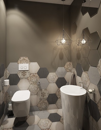 Nowoczesna łazienka z heksagonalnymi płytkami w odcieniach szarości i beżu, wisząca toaleta, umywalka na postumencie, geometryczne lampy wiszące i lustra w kształcie plastra miodu.