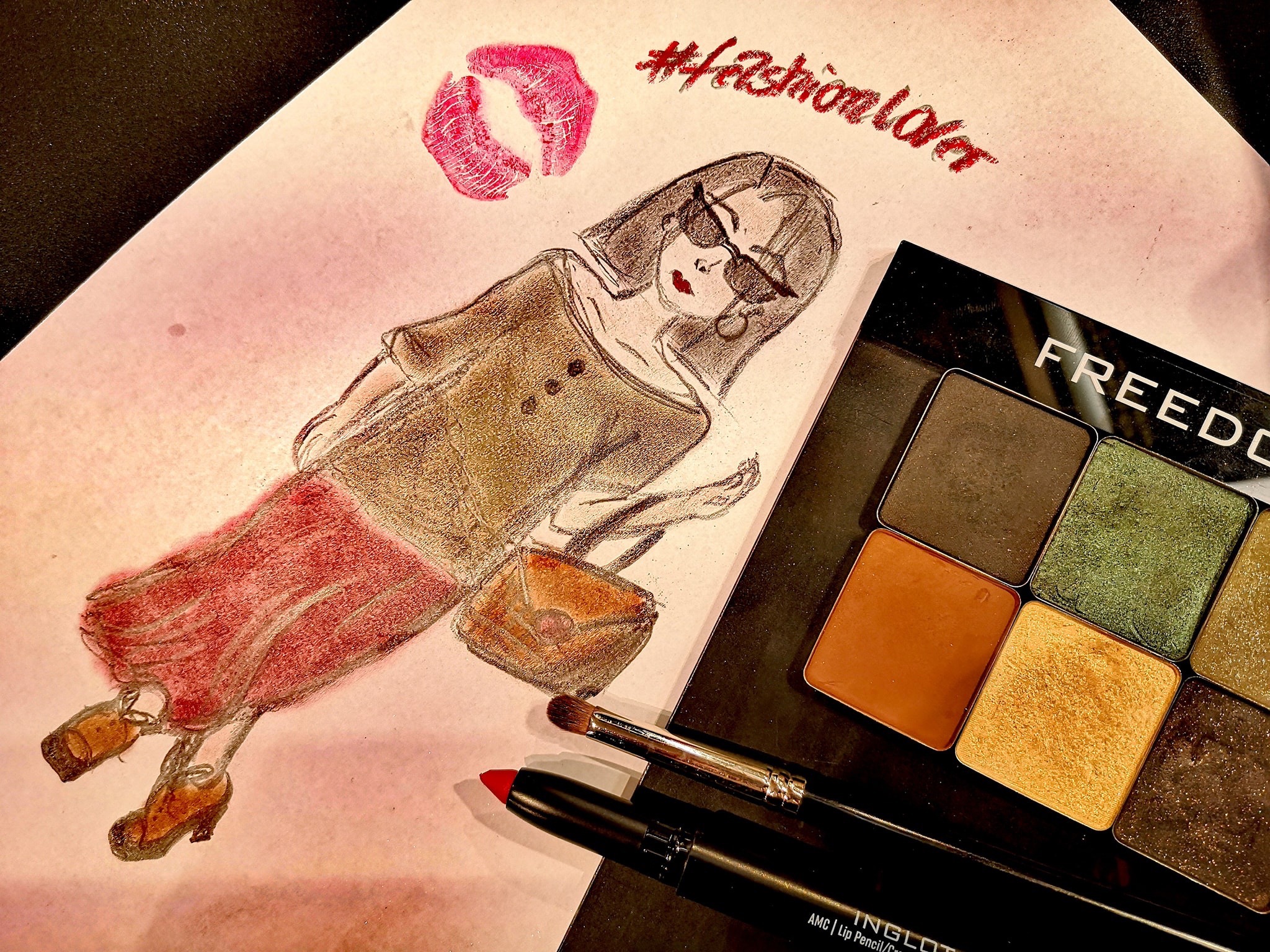 Szkic modnej kobiety w okularach, z torebką, obok odciśnięte usta, napis #fashionlover, paleta cieni do powiek i pędzel do makijażu.