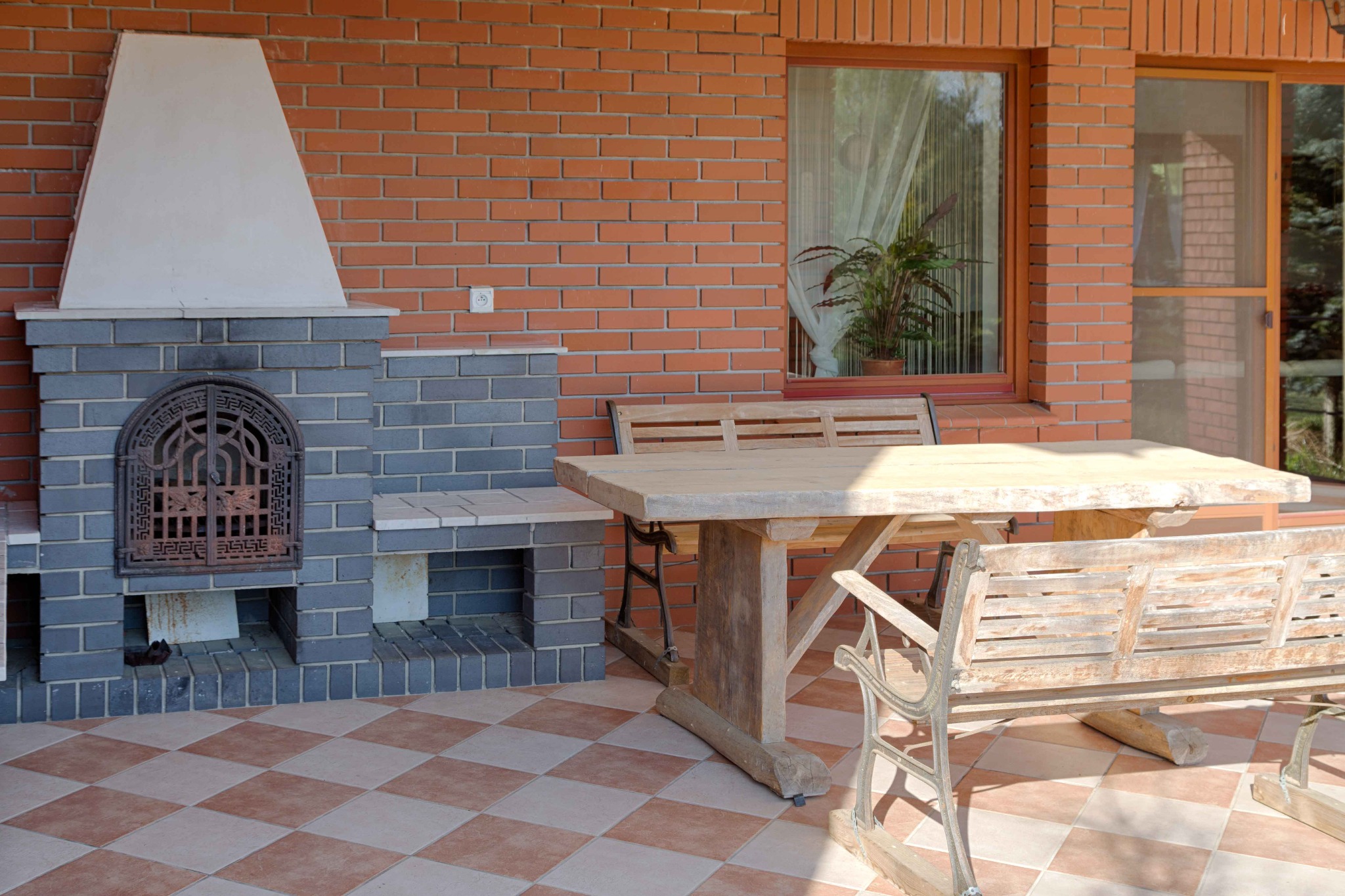 Zewnętrzny taras z ceglanym kominkiem, drewnianym stołem i ławkami w stylu rustykalnym.
