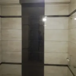 Wykończona ściana łazienki z beżowymi płytkami ceramicznymi i pionowym pasem ciemnych płytek z falistym wzorem, obramowana listwami dekoracyjnymi.