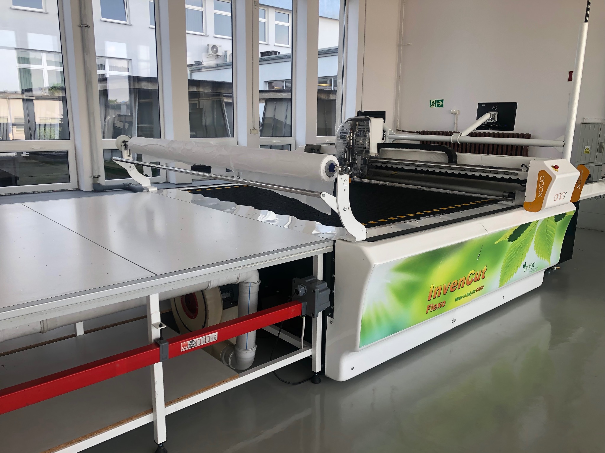 Profesjonalna krojownia: automat tnący InvenCut Flexo z rolką materiału, gotowy do precyzyjnego cięcia w jasnym, przestronnym pomieszczeniu z dużymi oknami.