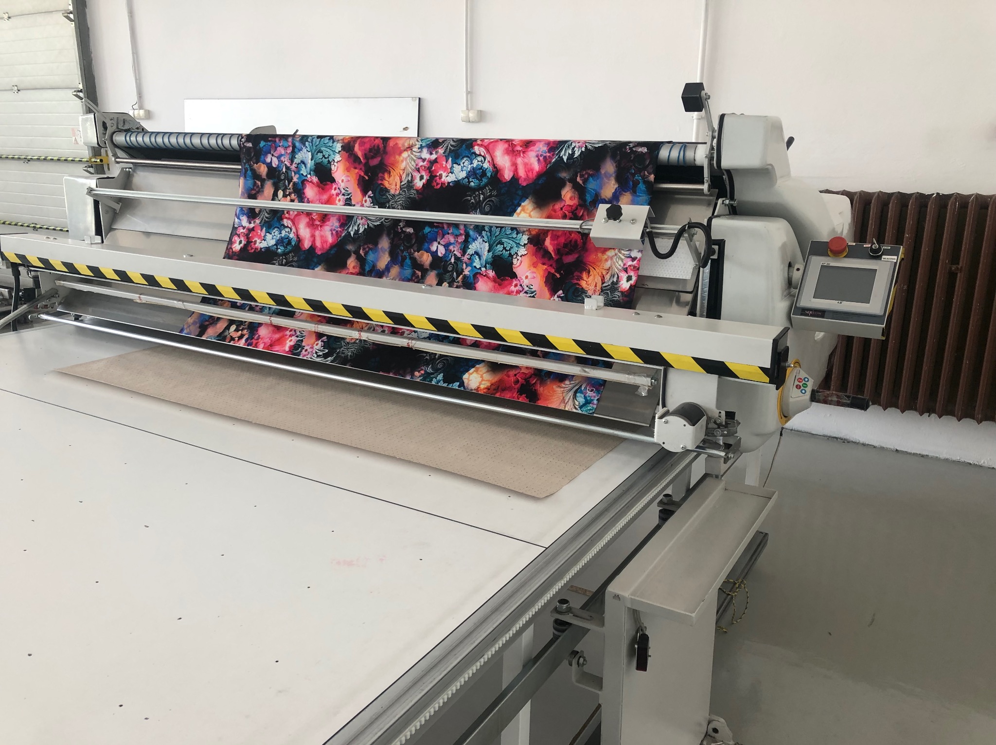Automat do cięcia tkanin z kolorowym wzorem kwiatowym, widoczny blat roboczy i panel sterowania. Precyzyjne cięcie materiałów w krojowni.