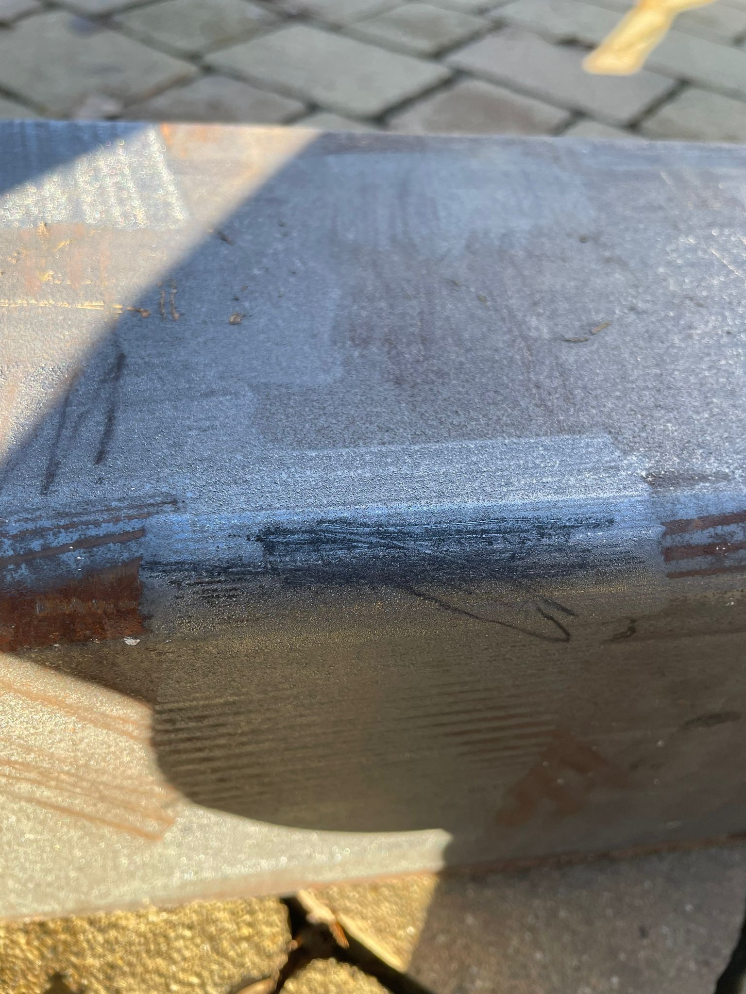Metalowy element po obróbce, widoczne ślady czyszczenia i przygotowania powierzchni. Fragment kostki brukowej w tle.
