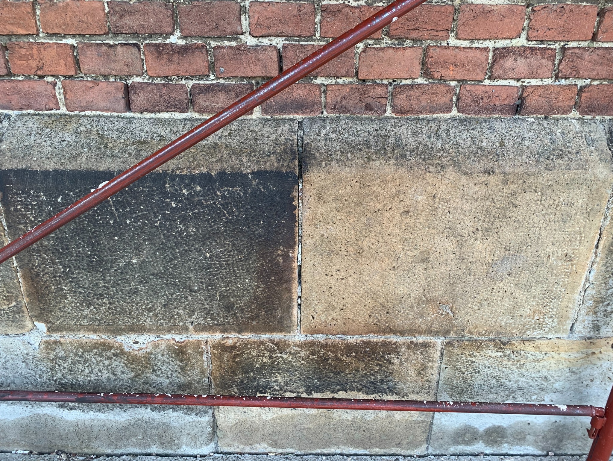 Ceglano-kamienna ściana z fragmentem metalowej konstrukcji. Po lewej stronie widoczny obszar po czyszczeniu, kontrastujący z zabrudzoną powierzchnią po prawej.