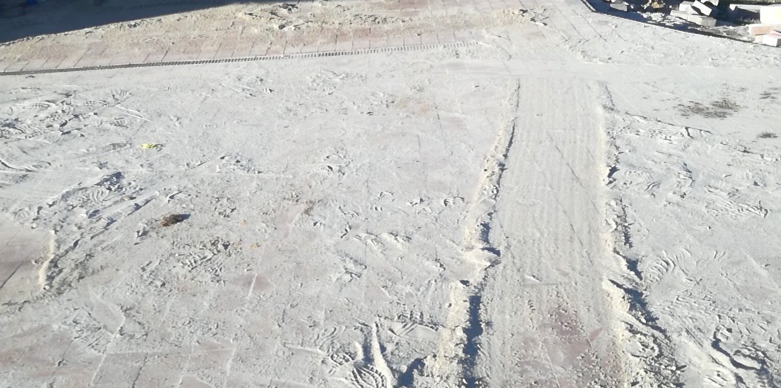 Przygotowanie podłoża pod kostkę brukową: wyrównany piasek z widocznymi śladami stóp i fragmentami ułożonej kostki w tle.