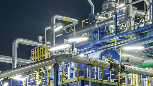 Złożona instalacja przemysłowa z rurami, zaworami i elementami konstrukcyjnymi, oświetlona sztucznym światłem w nocnej scenerii.