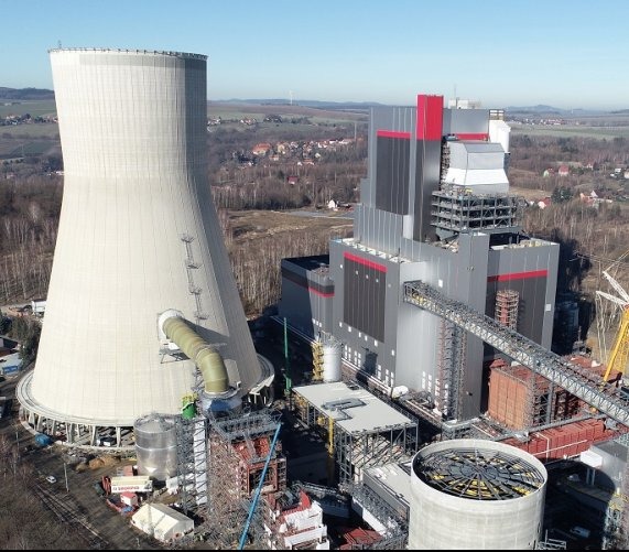 Zdjęcie z lotu ptaka przedstawia elektrownię węglową z charakterystyczną chłodnią kominową w kształcie hiperboloidy, połączoną rurociągiem z budynkiem głównym o stalowo-szarej elewacji z czerwonymi...