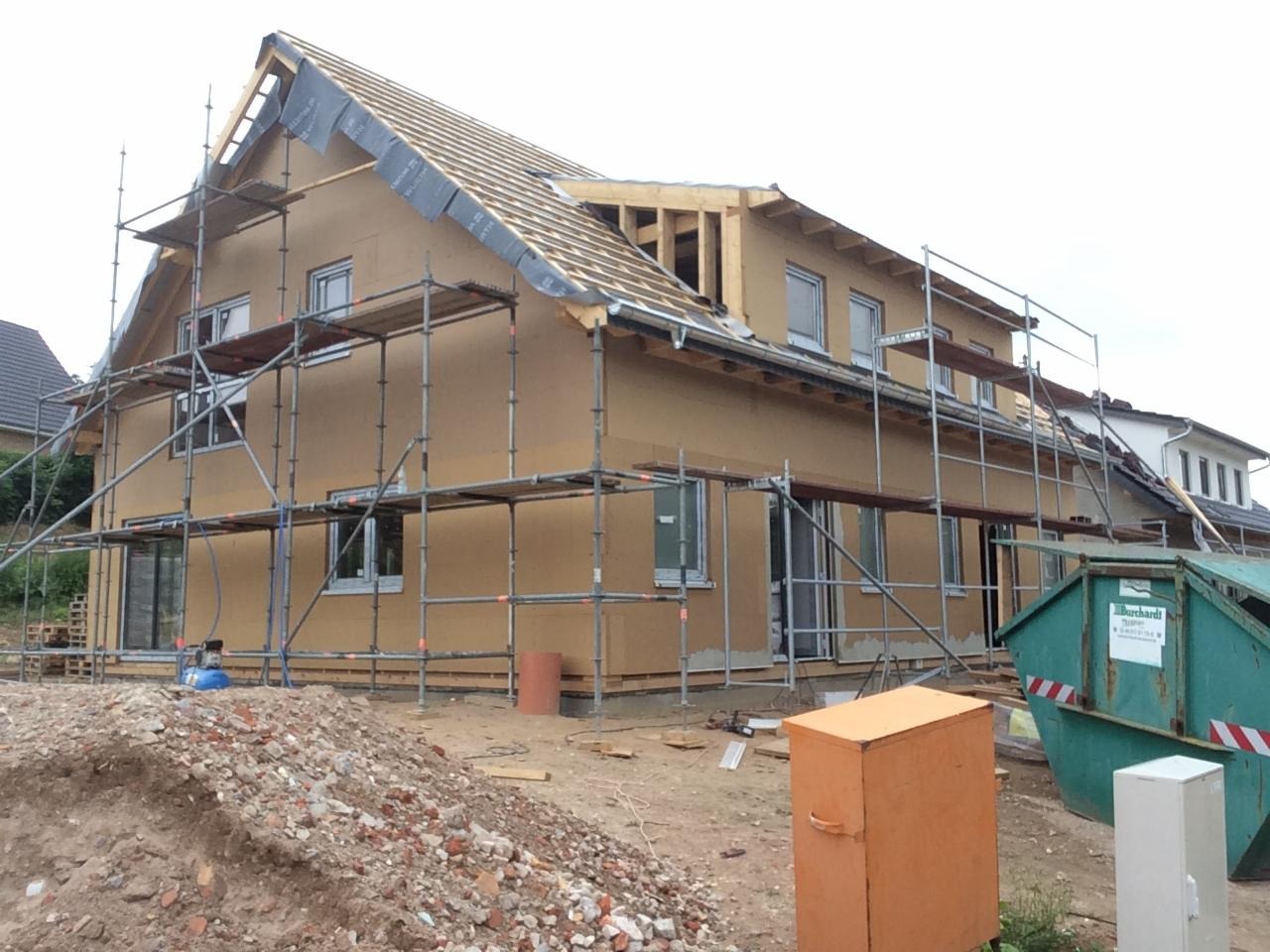 Dom w trakcie ocieplania elewacji i budowy dachu, widoczne rusztowania, gruz i kontener na odpady budowlane.