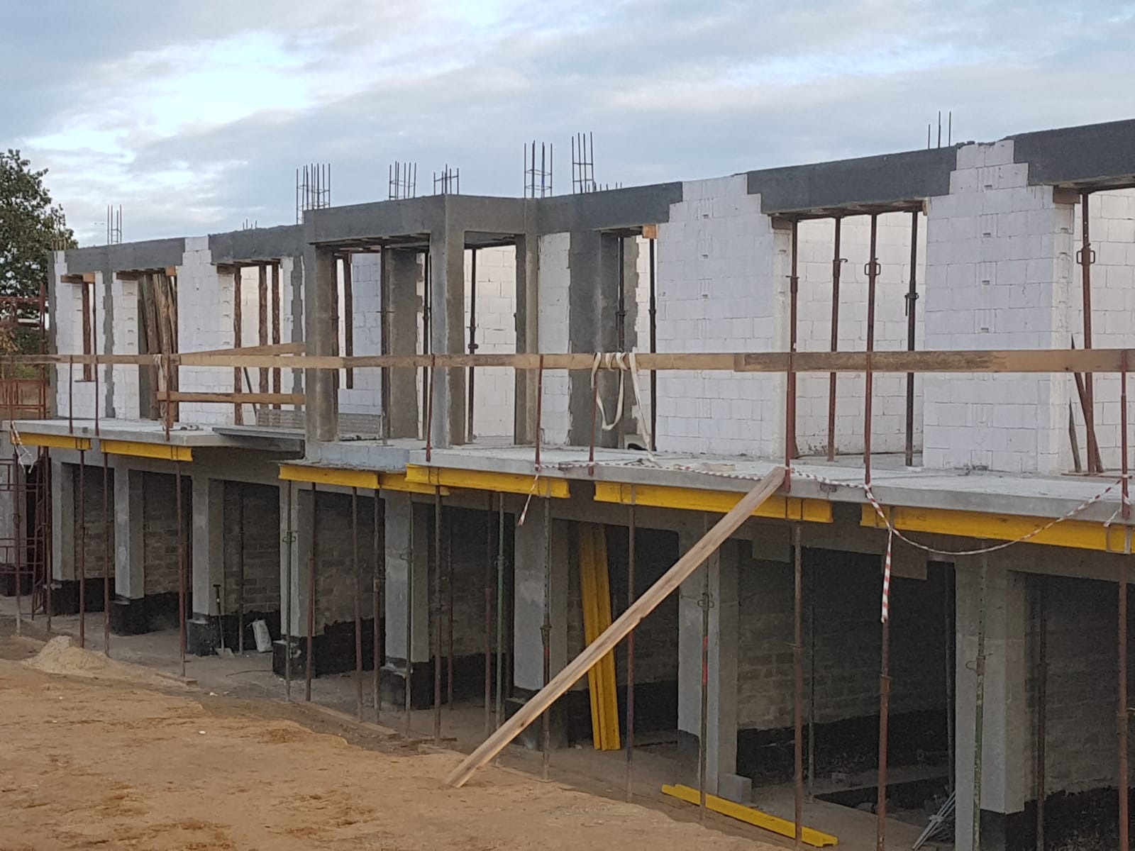 Wznoszenie ścian budynku wielorodzinnego z betonu komórkowego, widoczne szalunki i podpory stropu, zbrojenia nad oknami, plac budowy z piaskiem.